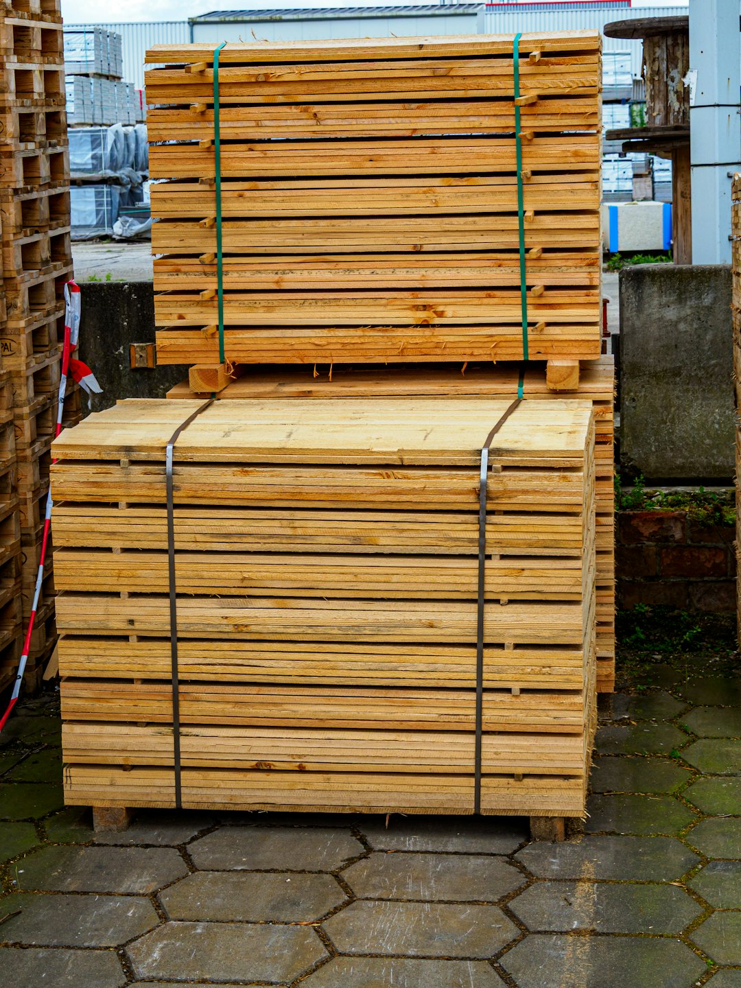Two stacks of bundled wooden planks on concrete pavers.