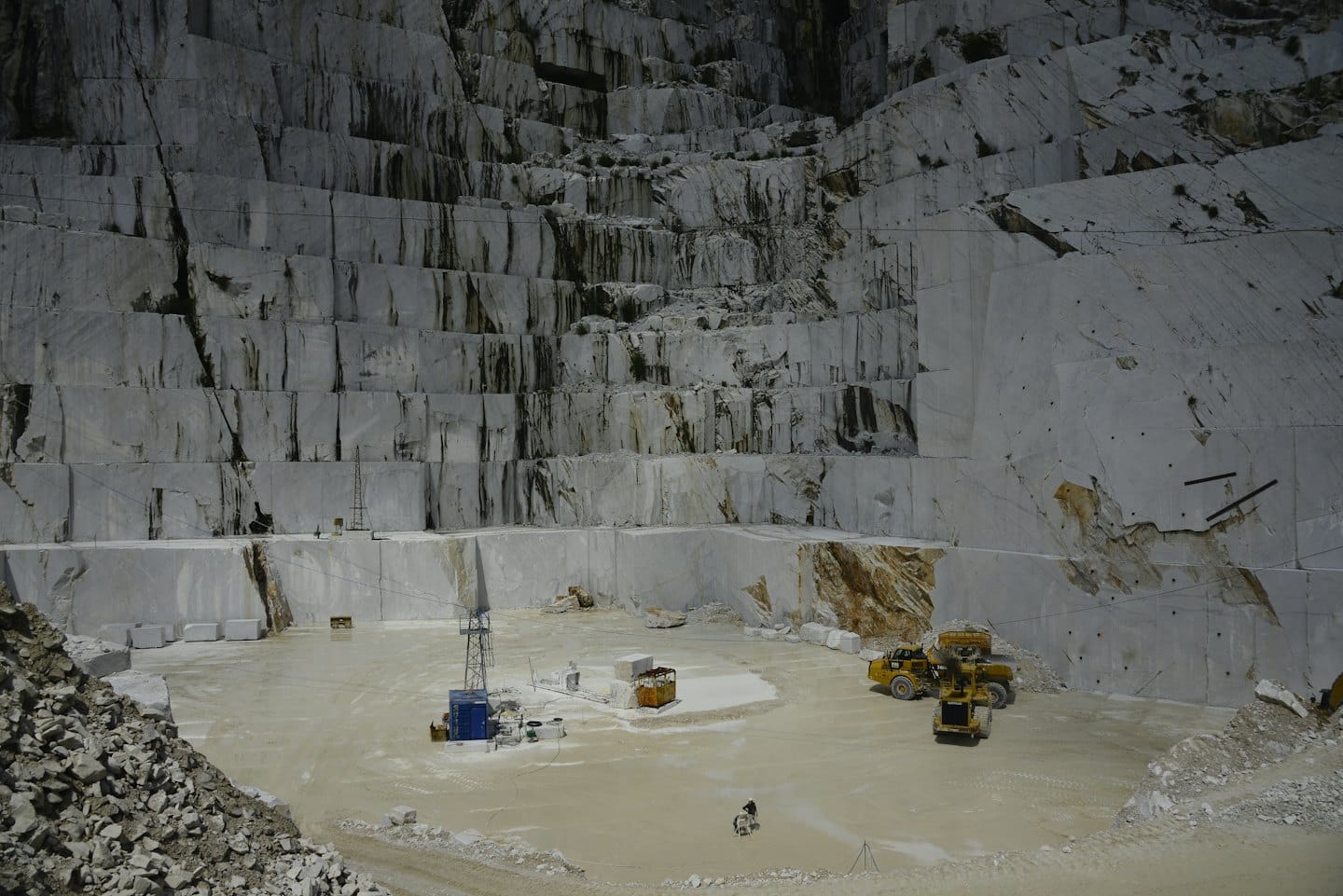 Yellow heavy machinery operates inside a large open-pit marble quarry.