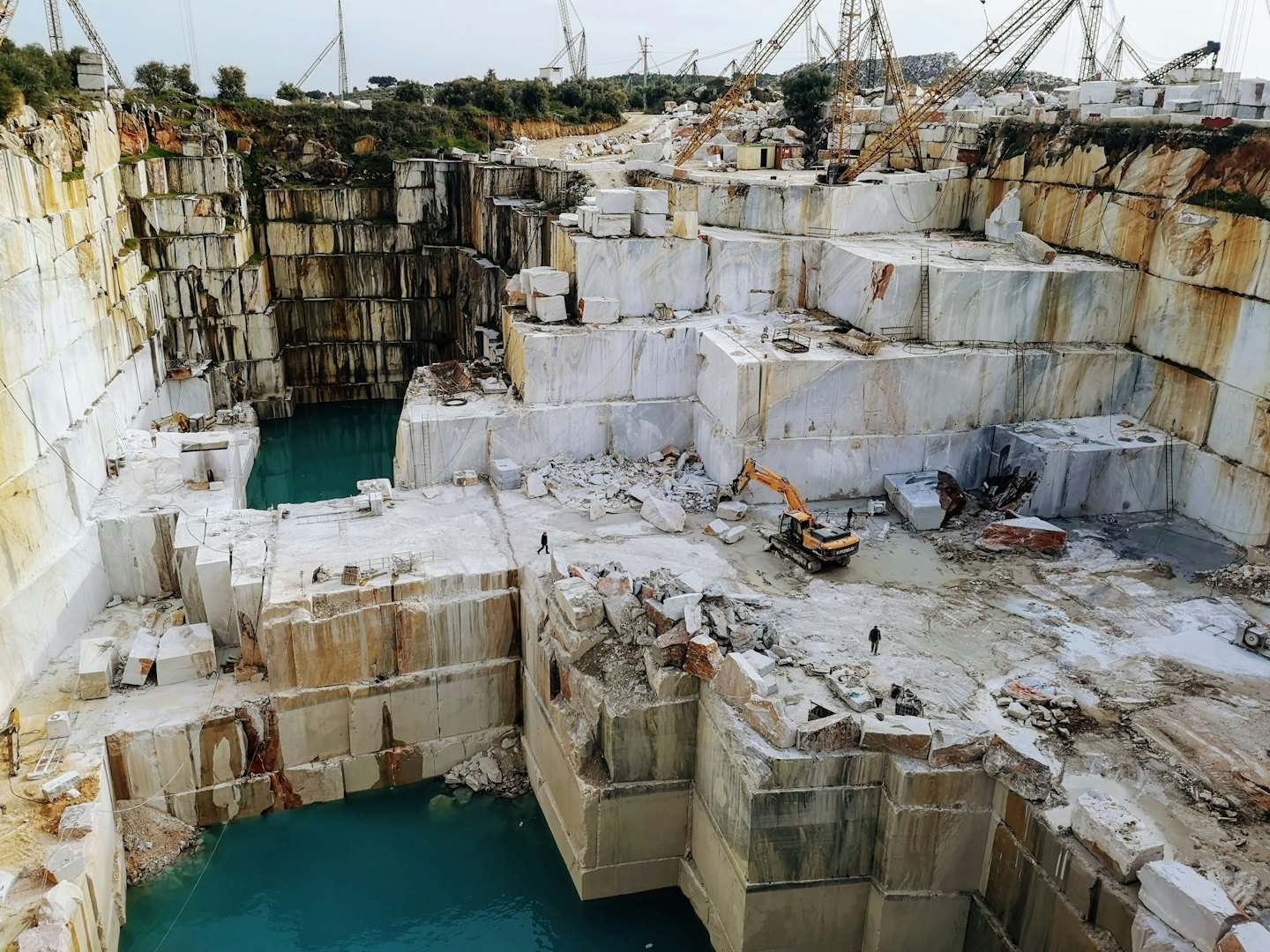 Industrial machinery operates within a vast open-pit marble quarry.