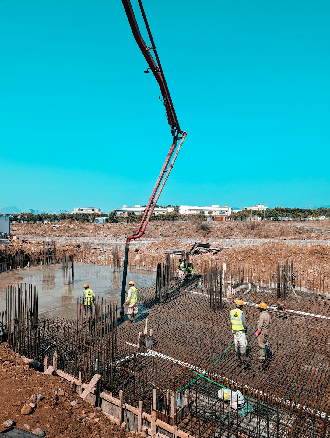 Construction workers pour concrete using a pump arm on a sunny day.